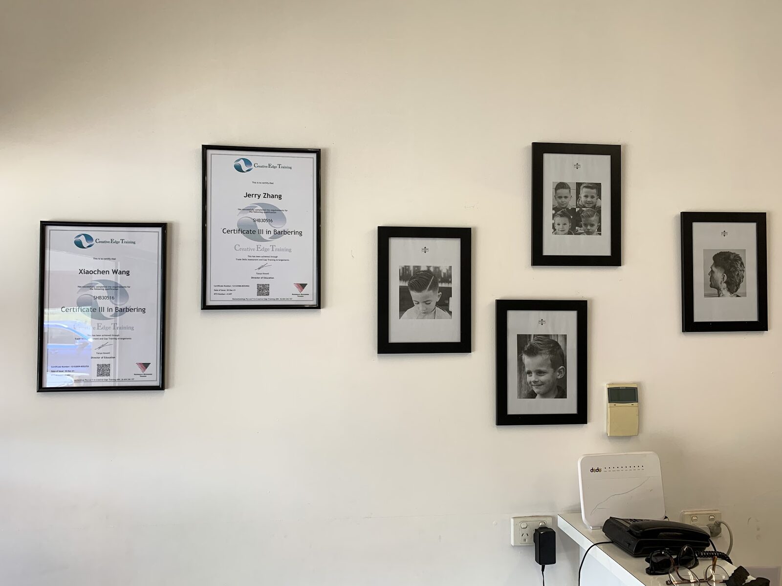 Framed barbering certificates and haircut photos on the shop wall